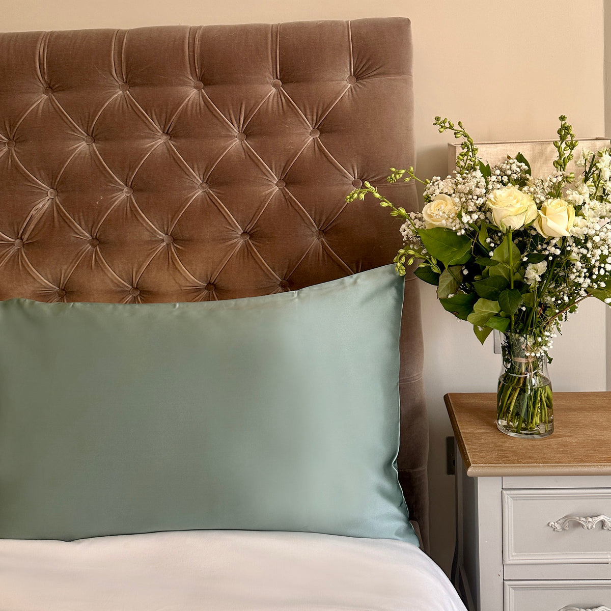 Duck egg blue mulberry silk pillowcases on a velvet headboard with fresh flowers on the bedside table