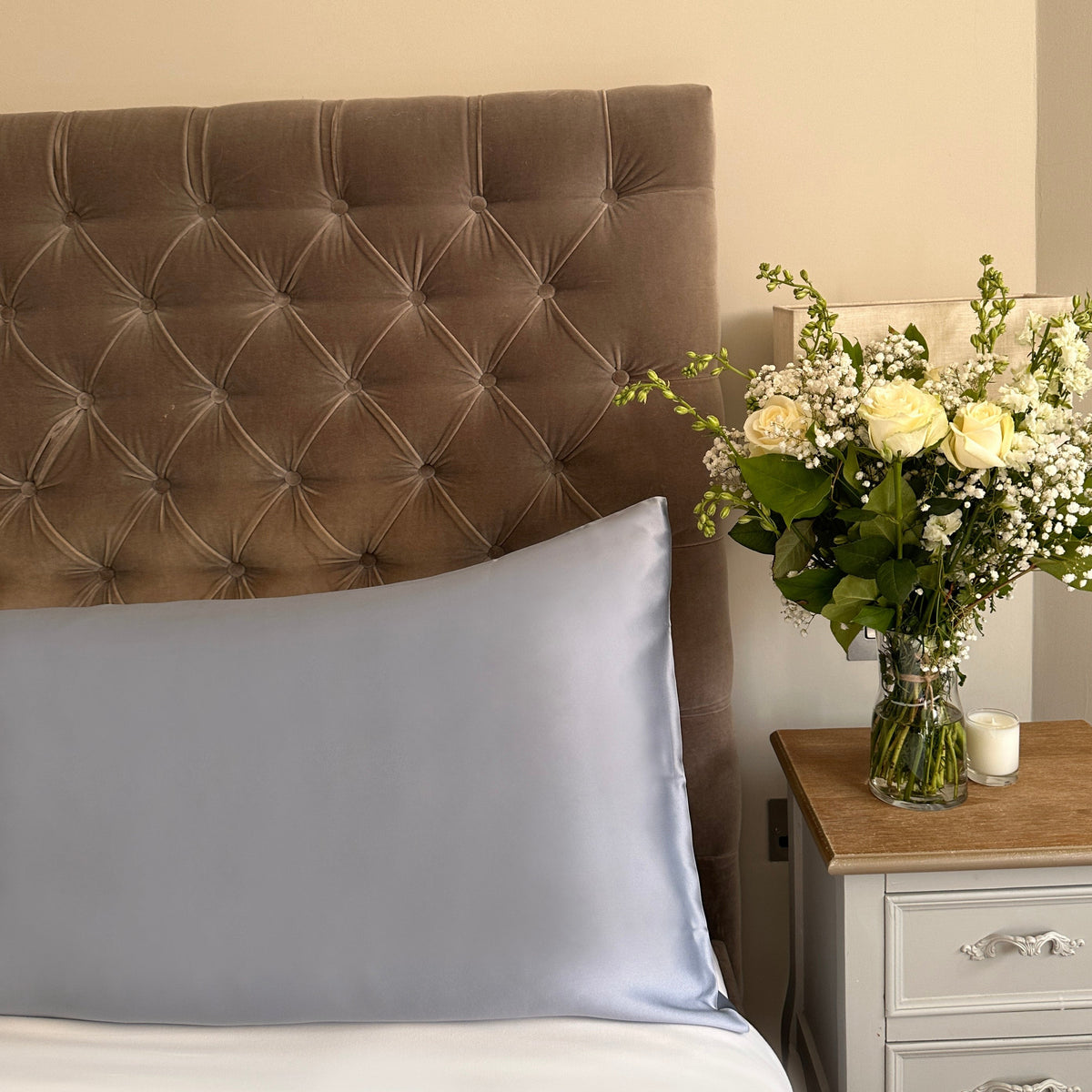 Steel blue mulberry silk pillowcases on a velvet headboard with fresh flowers on the bedside table