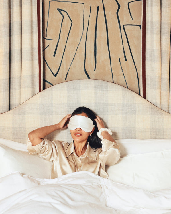 Pearl white silk eye mask over eyes arms up in bed