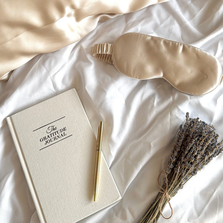 Champagne silk pillowcase and silk eye mask on white bedding with a journal and lavender